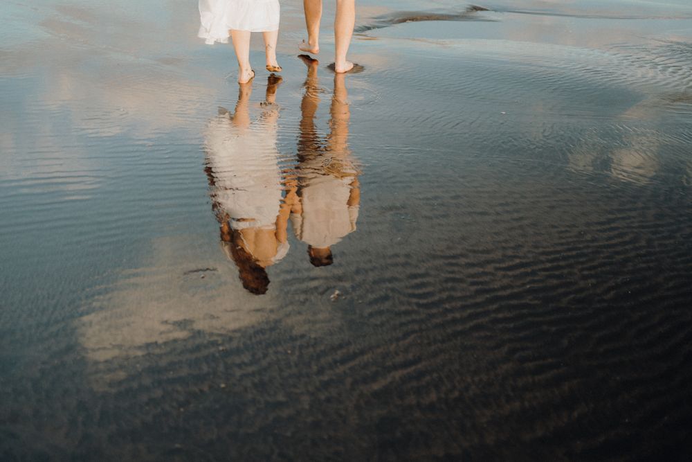 Feet reflected in wet sand at the beach during golden hour.
