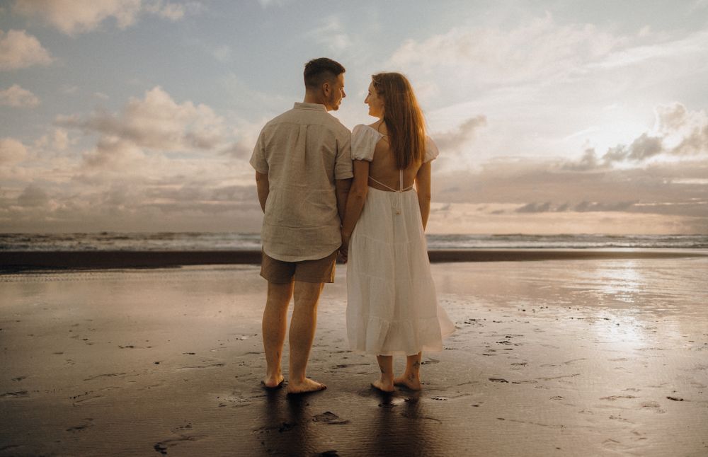 Couple standing together on beach at sunset watching the ocean waves.