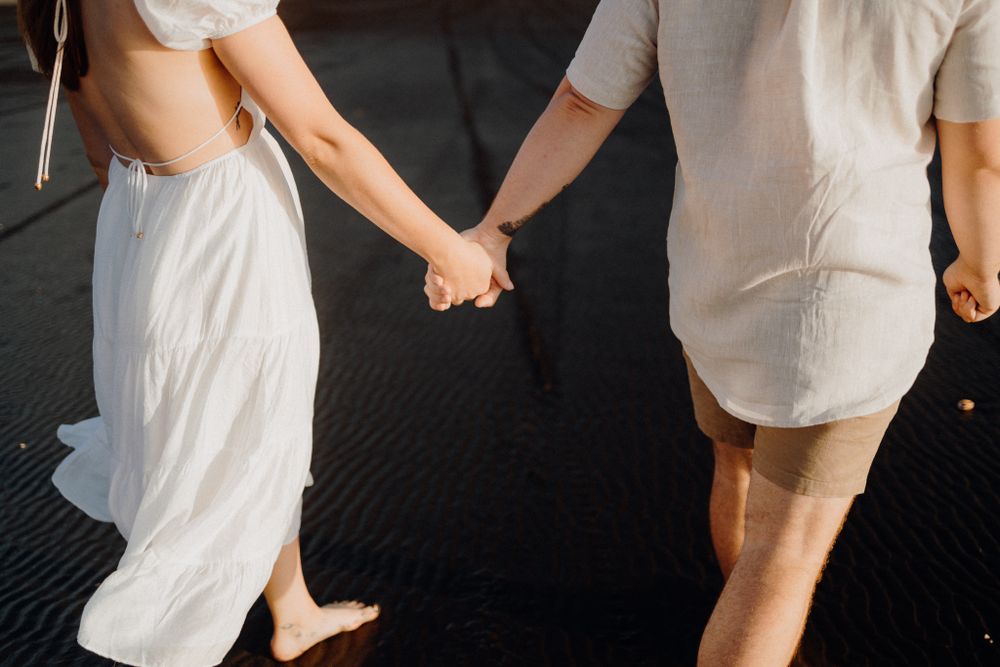 A couple holding hands on a dark surface, shown from waist down in white summer clothing.