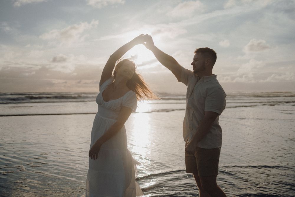 Romantic dance pose with raised arms silhouetted against sunset on beach.