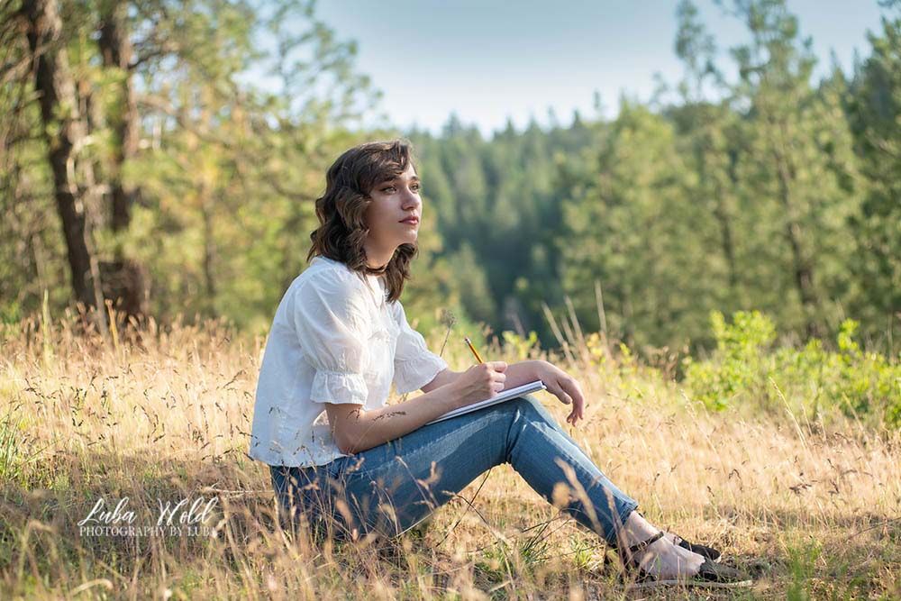 high school senior girl sitting on a hill in Post Falls outdoor studio dreaming or drawing photographer luba wold