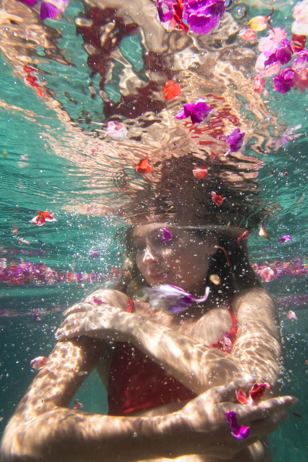 girl hugs herself underwater surrounded by flowers