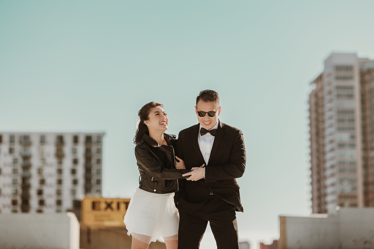 A romantic rooftop photoshoot featuring a couple in formal attire against an urban backdrop with high-rise buildings.