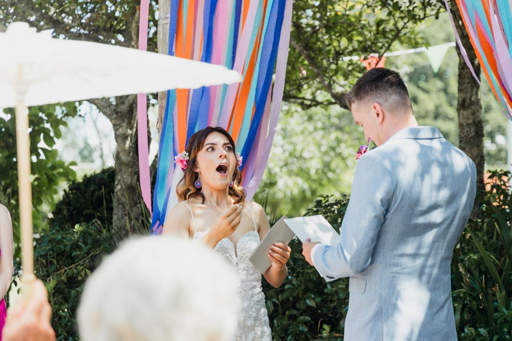 A joyful wedding ceremony moment with colorful streamers as the couple exchanges vows in an outdoor garden setting.