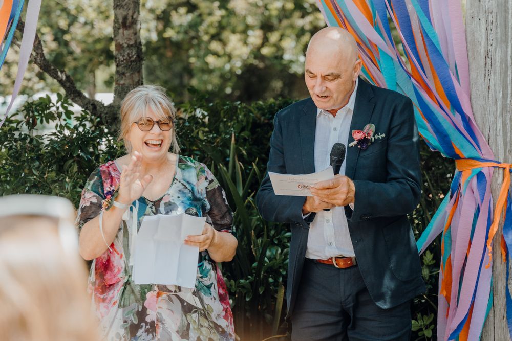 Wedding speakers sharing moment under colorful streamers during outdoor ceremony.