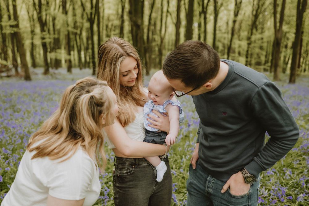 Three people sharing a tender moment together among blooming bluebells in a spring forest.
