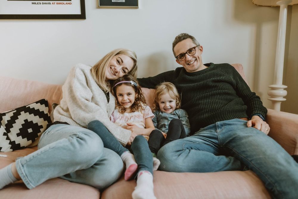 A relaxed family lounges together on a couch in casual outfits while enjoying quality time at home.