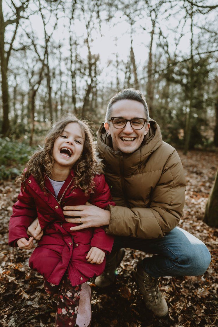 A joyful outdoor portrait of a parent and child laughing together in a wooded setting during autumn.