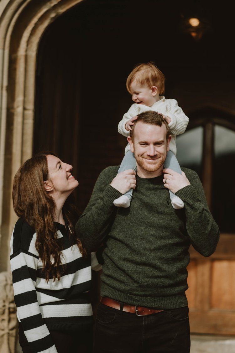 A family of three shares a joyful moment together as they pose in front of a wooden doorway.