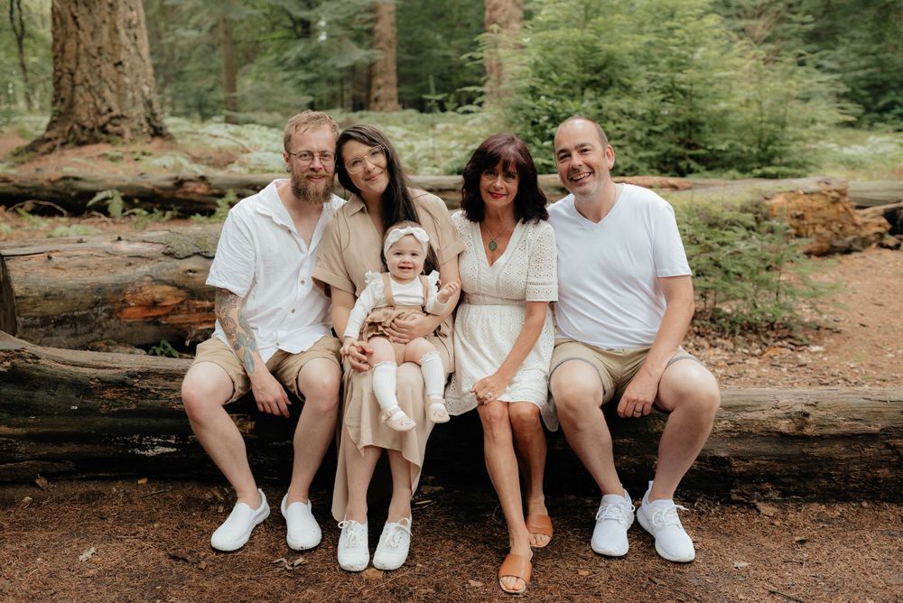 A group in coordinated neutral outfits sits together on a fallen tree trunk in a peaceful forest setting.