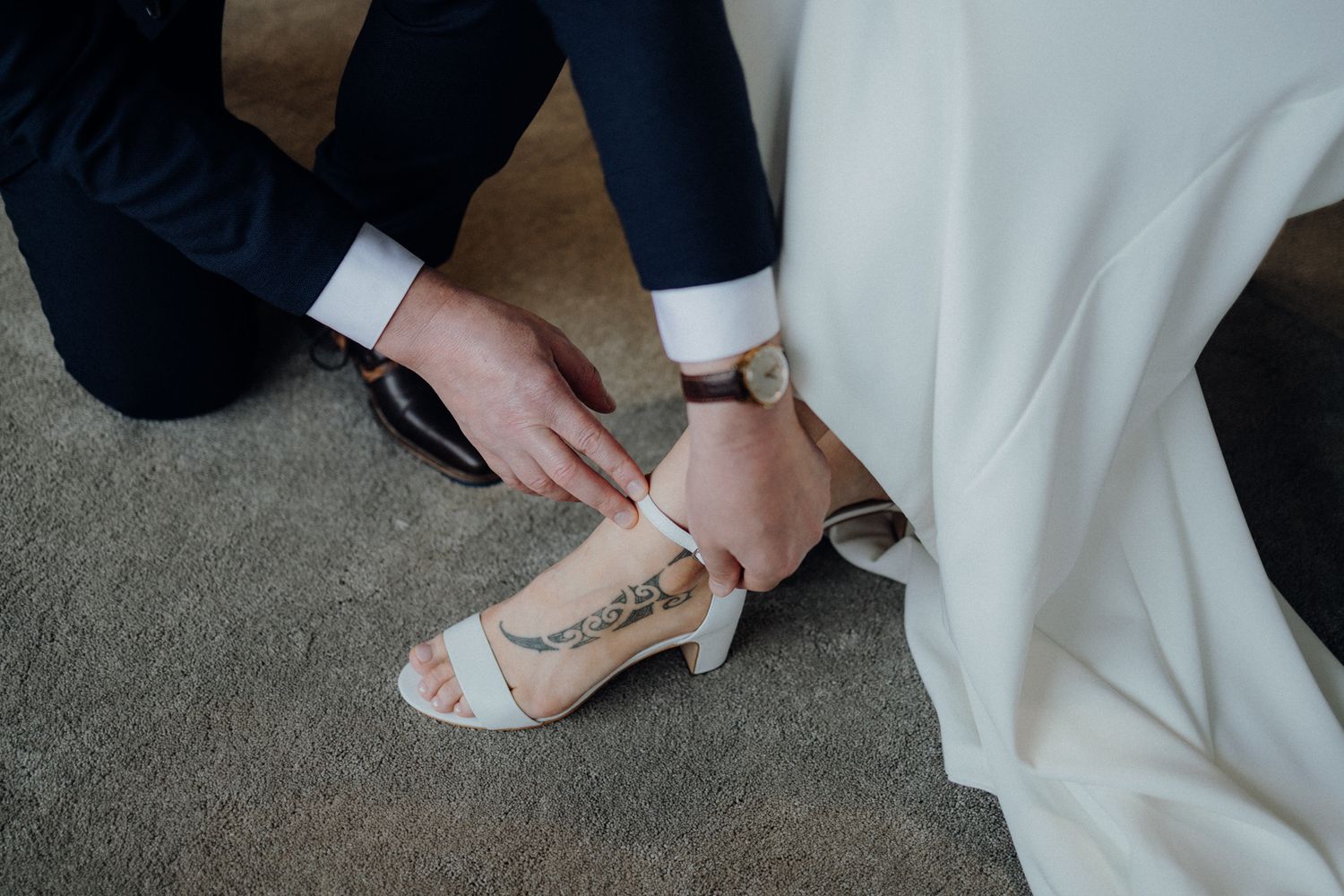 Close up of hands fastening straps on white wedding sandals against carpet.
