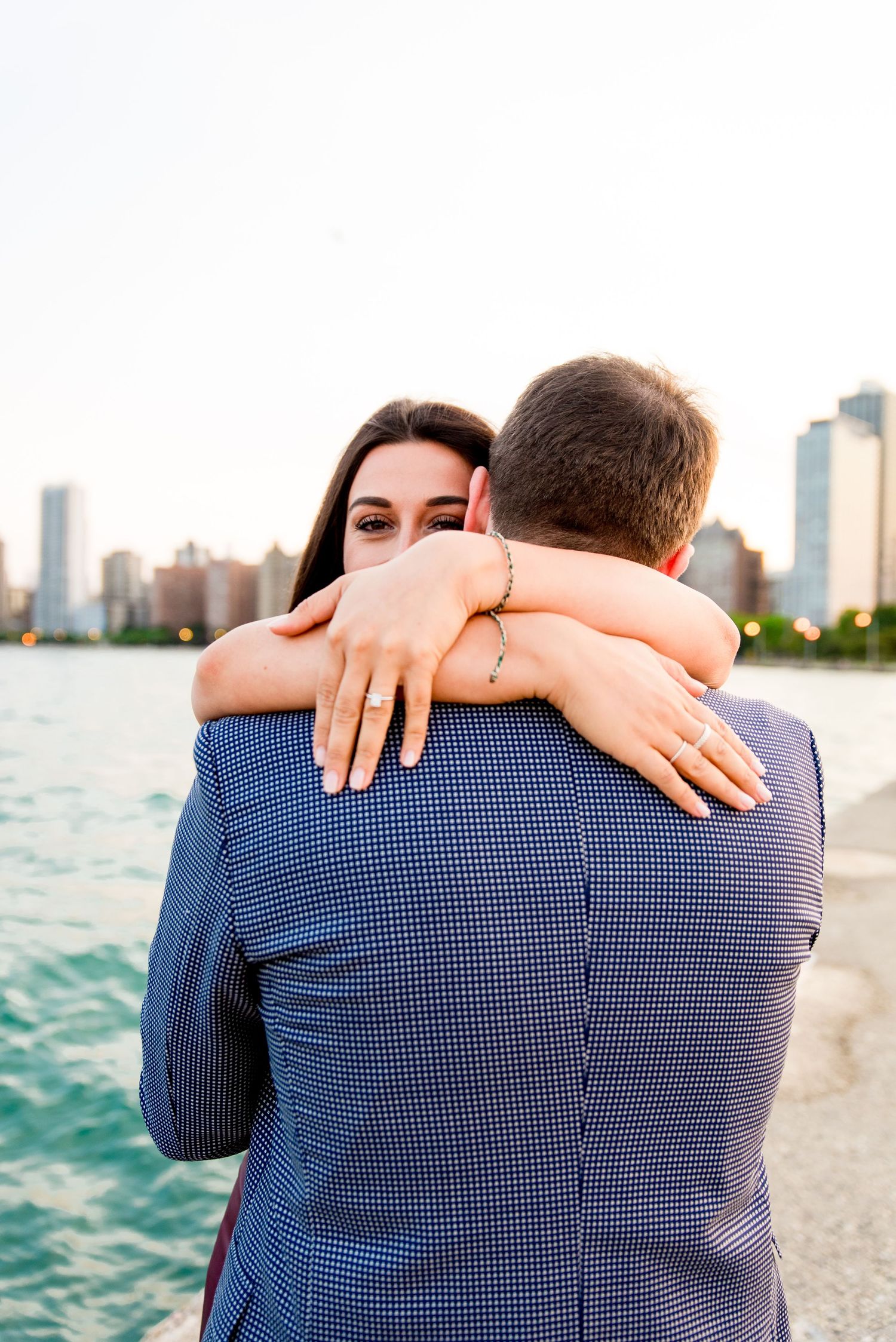 woman hugging new fiance showing off her ring and peeking over his shoulder