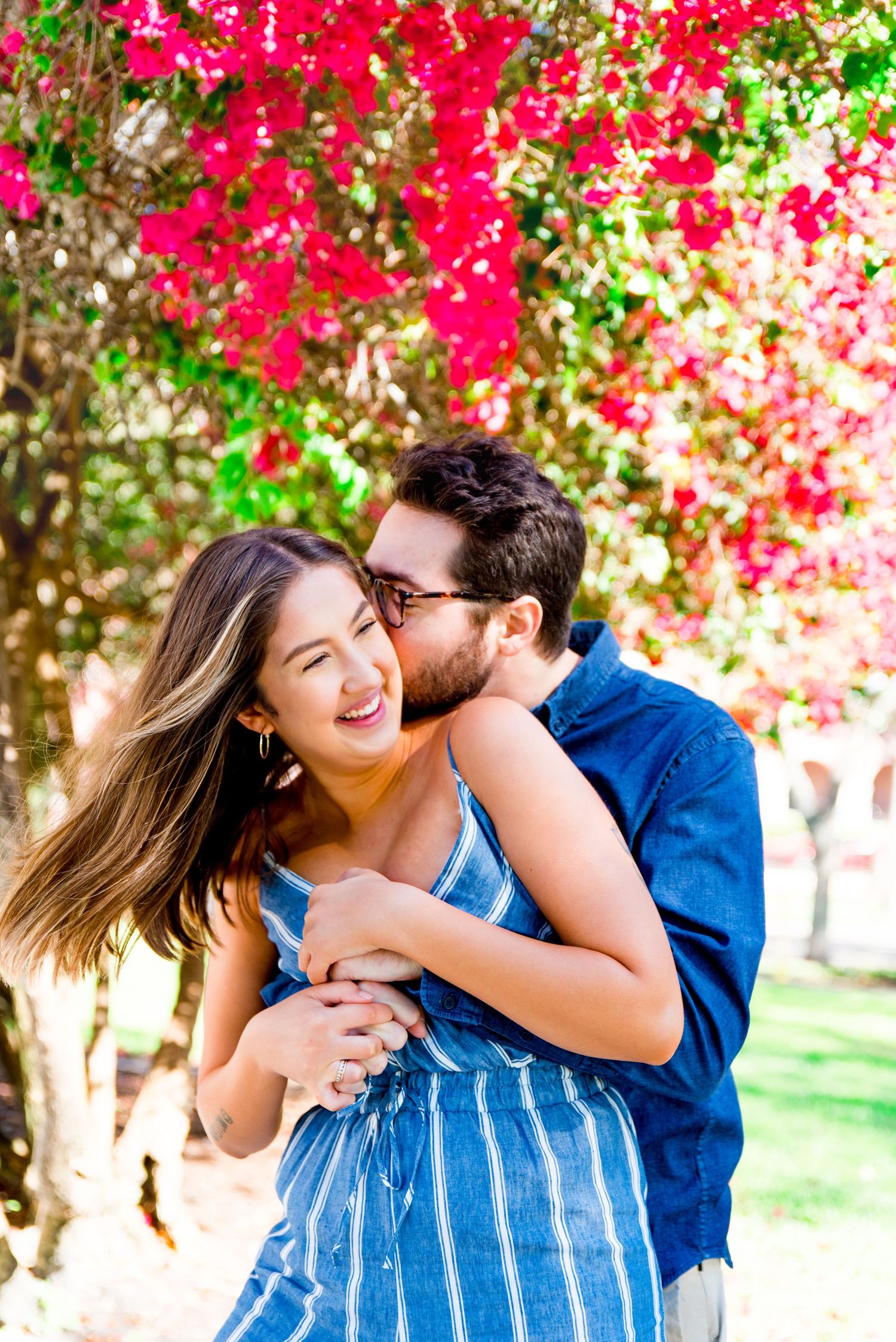 young man kissing woman's neck under pink flower tree at Vinoy Park, St Pete engagement photos