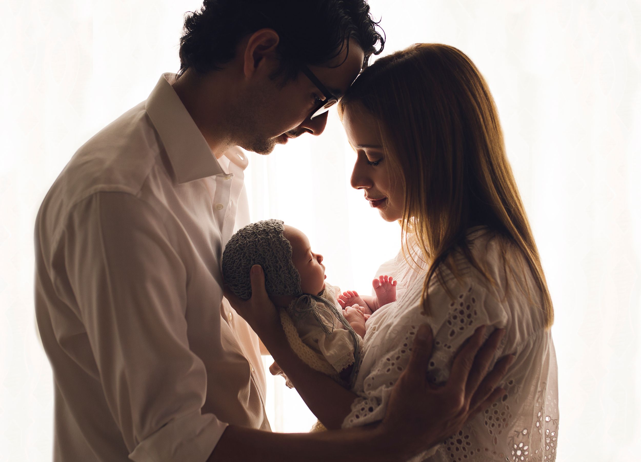 Mom and dad hold their newborn baby girl close backlit image