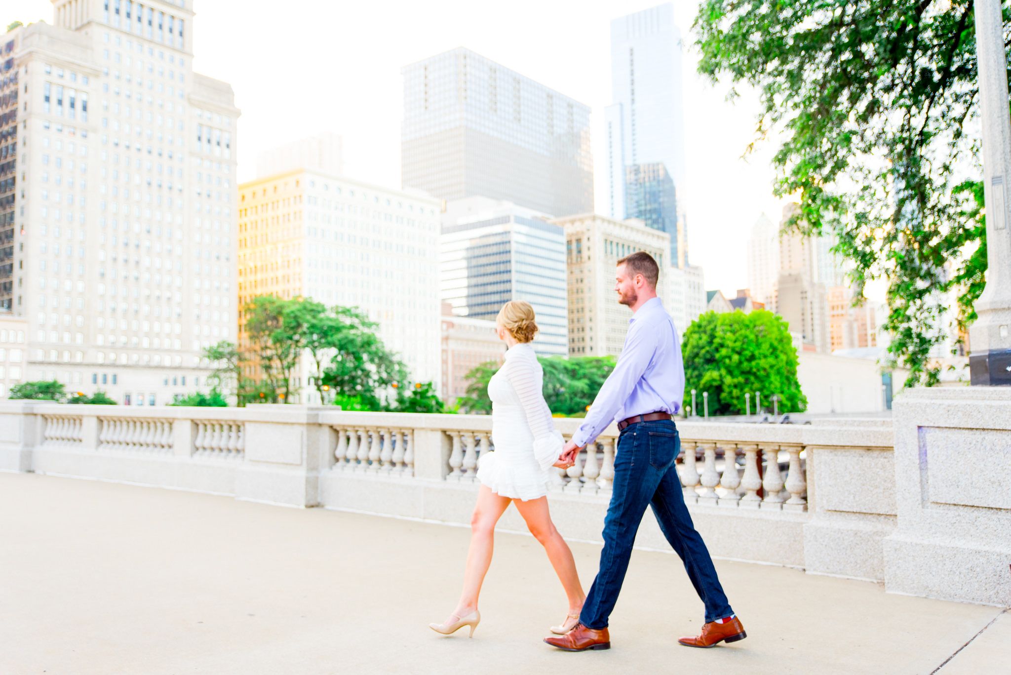 woman in white dress leading man through Chicago at sunset for engagement pictures