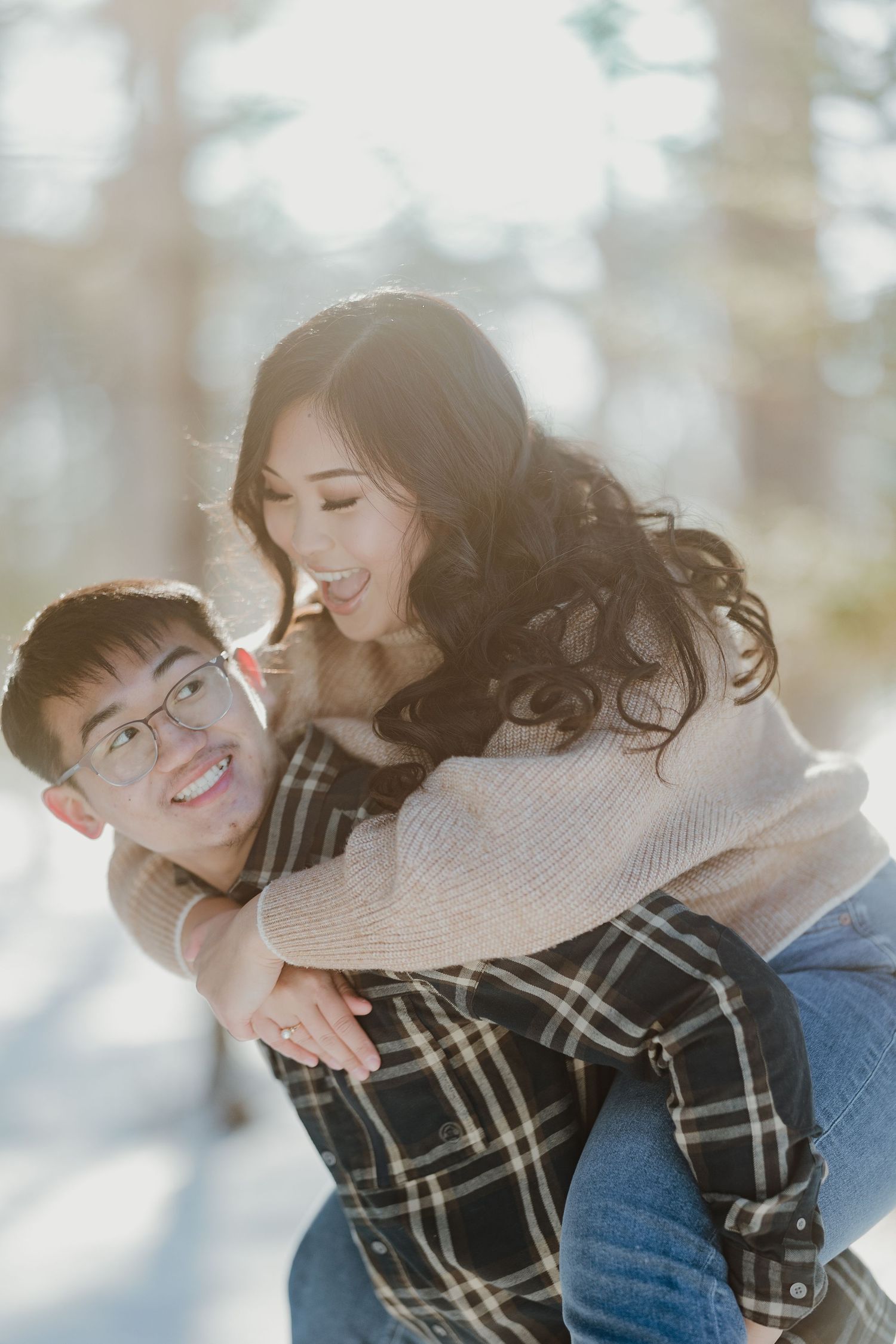 A couple sharing a playful piggyback ride moment in a snowy winter forest setting.