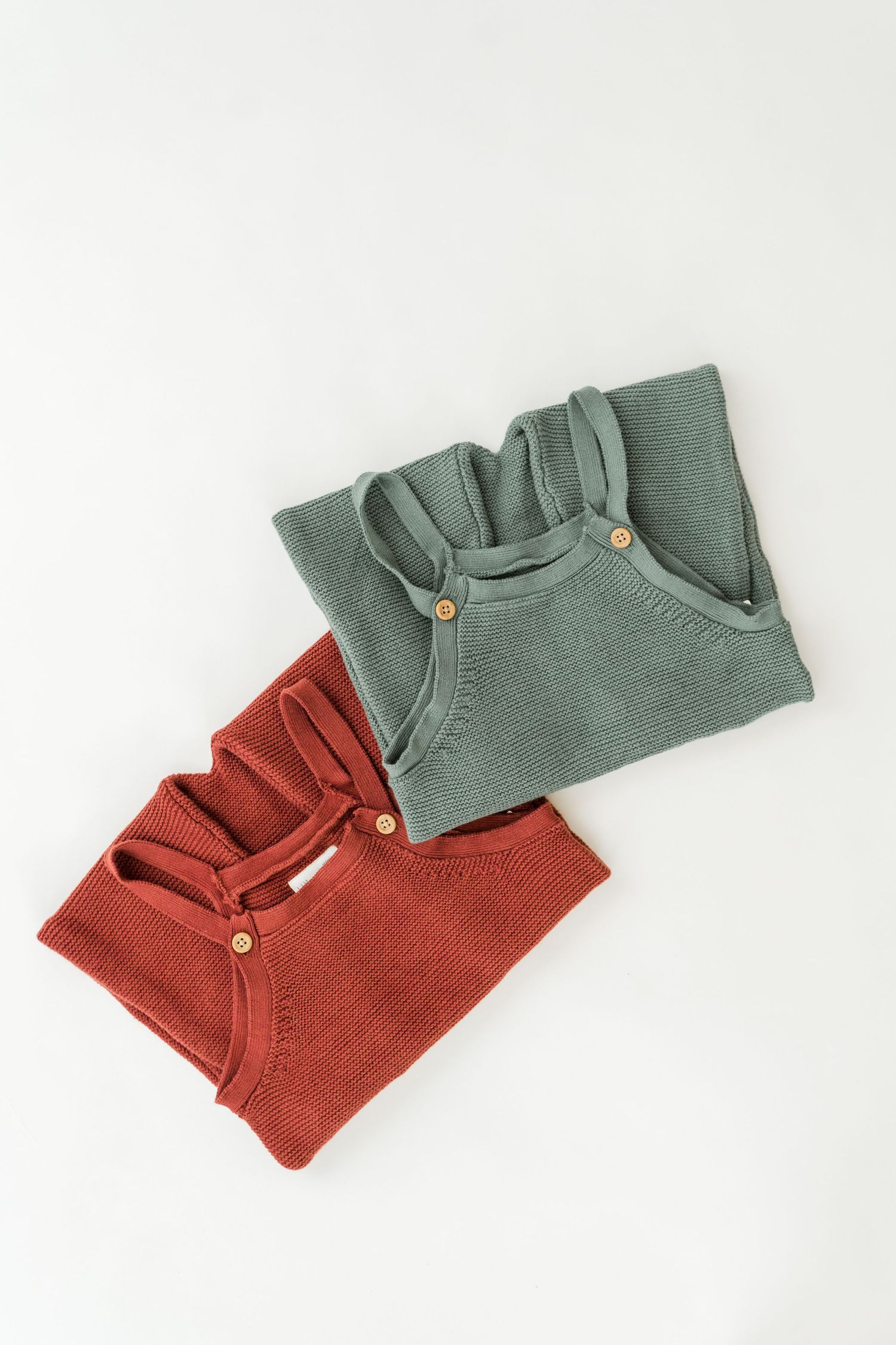 Two folded knit sweaters in sage green and rust red displayed on white background.