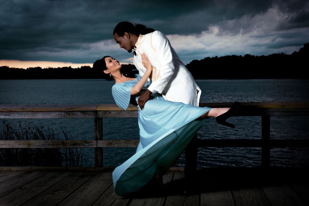Dancing couple in dramatic pose on wooden pier with moody storm clouds at sunset.