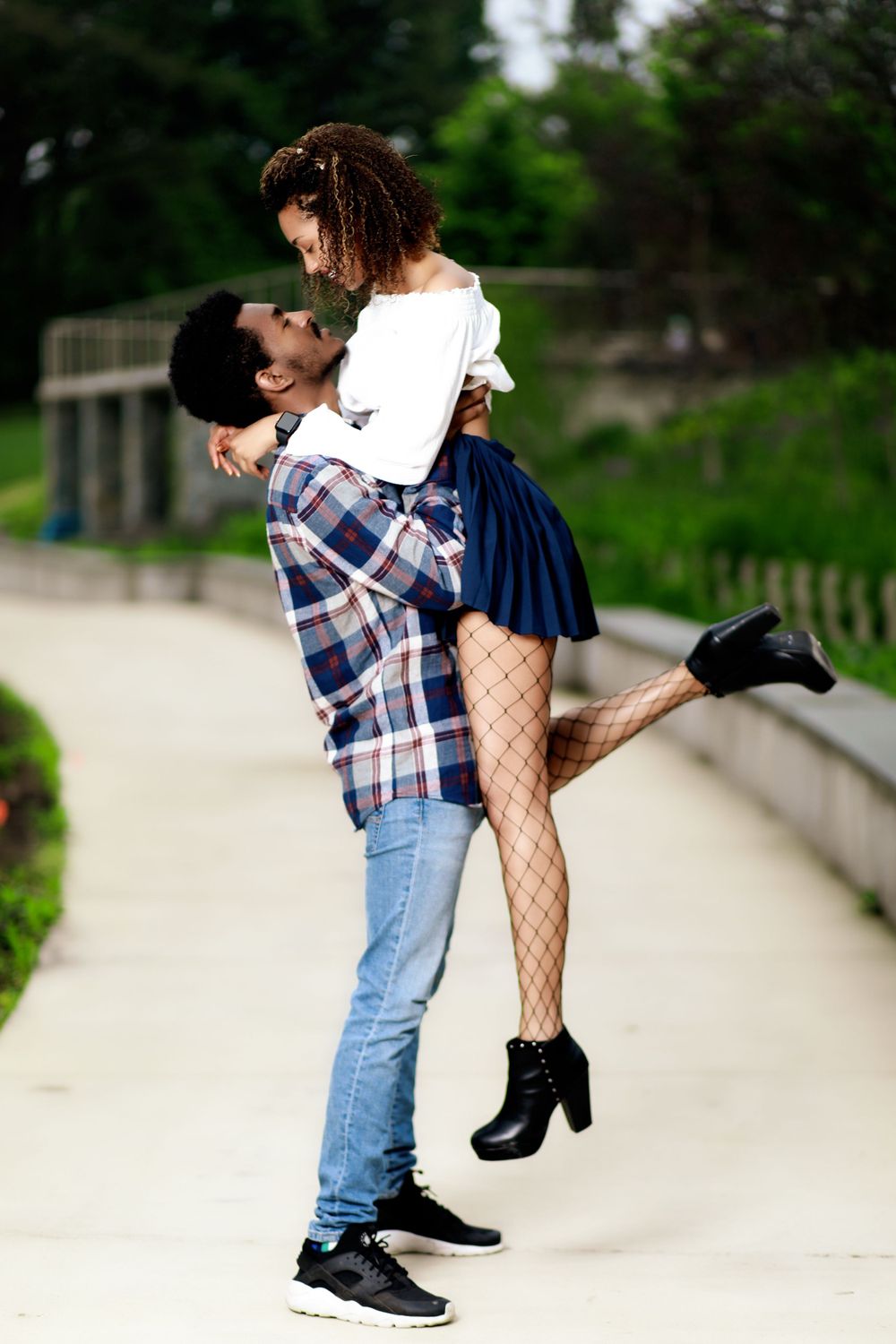 A romantic couple embraces playfully on a garden path surrounded by greenery.