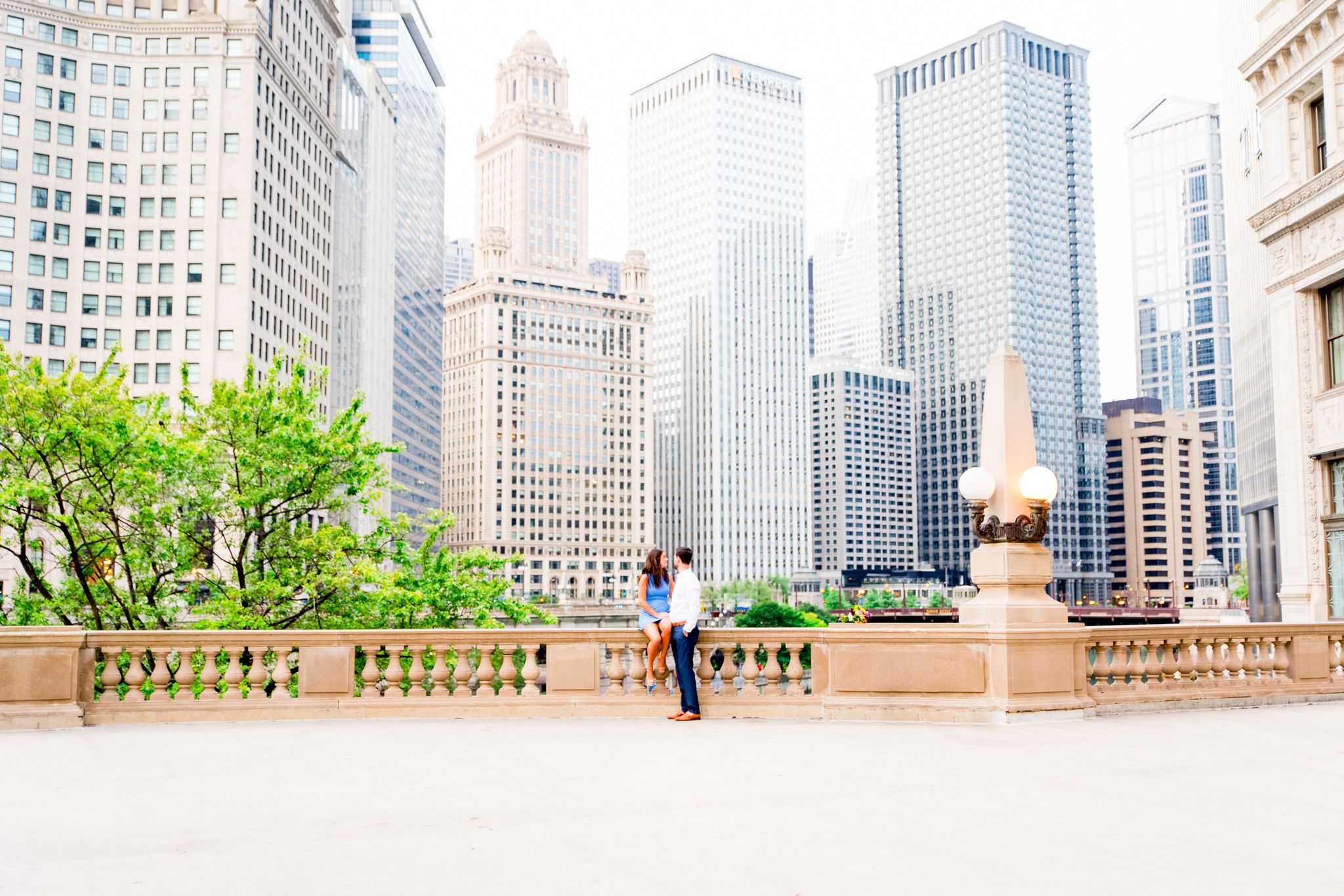 woman with brown hair in blue dress sitting near chicago riverwalk and wrigley building with fiance at sunrise