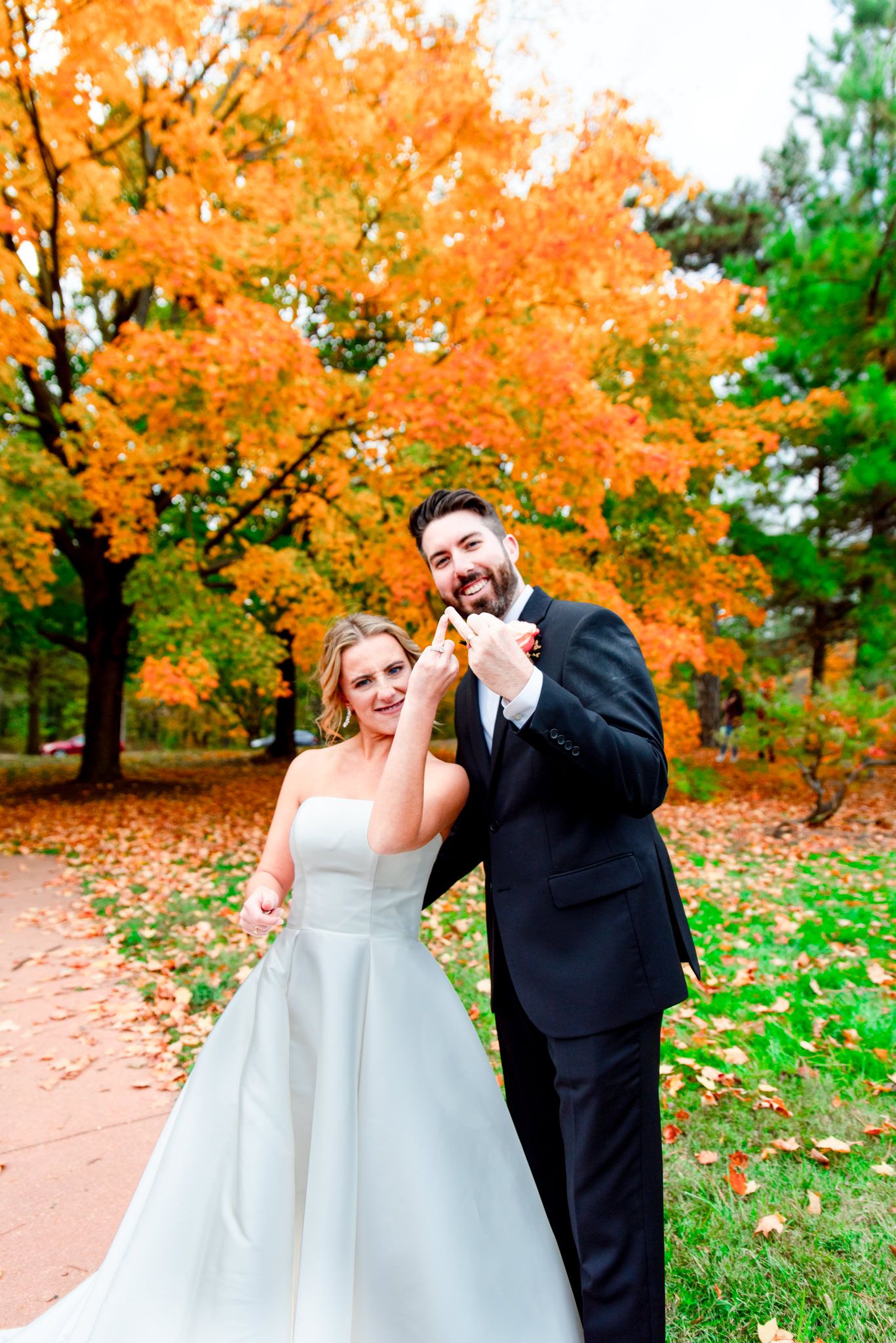bride and groom hold up ring fingers in front of bright orange tree