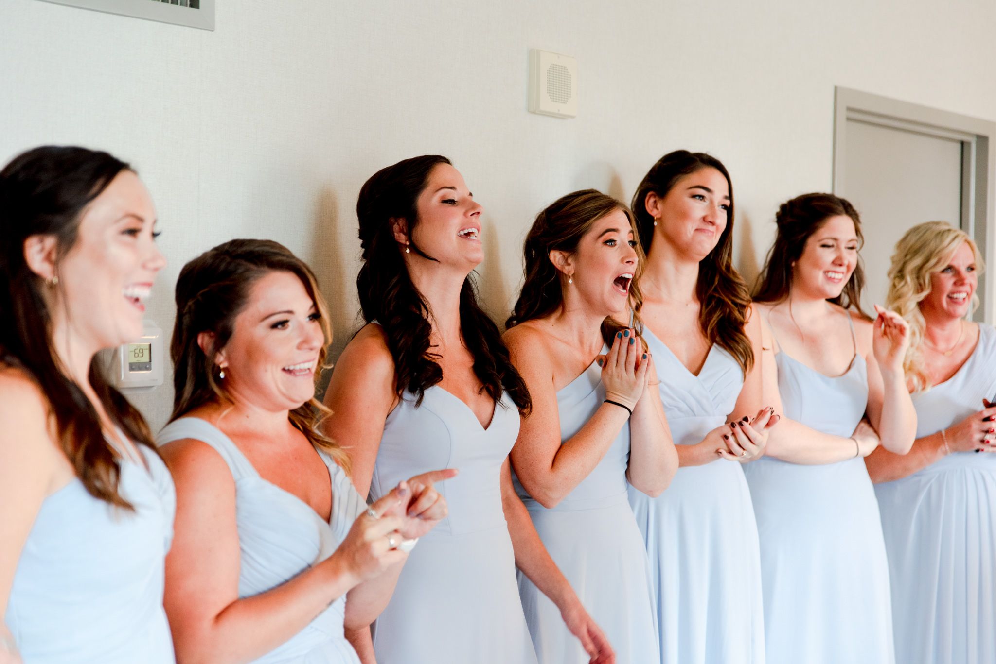 7 bridesmaids in light blue dresses smiling and clapping after seeing the bride