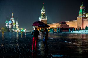 Two men struggle in rain storm to take photo of St. Basil's Cathedral in the Red Square Moscow Russia