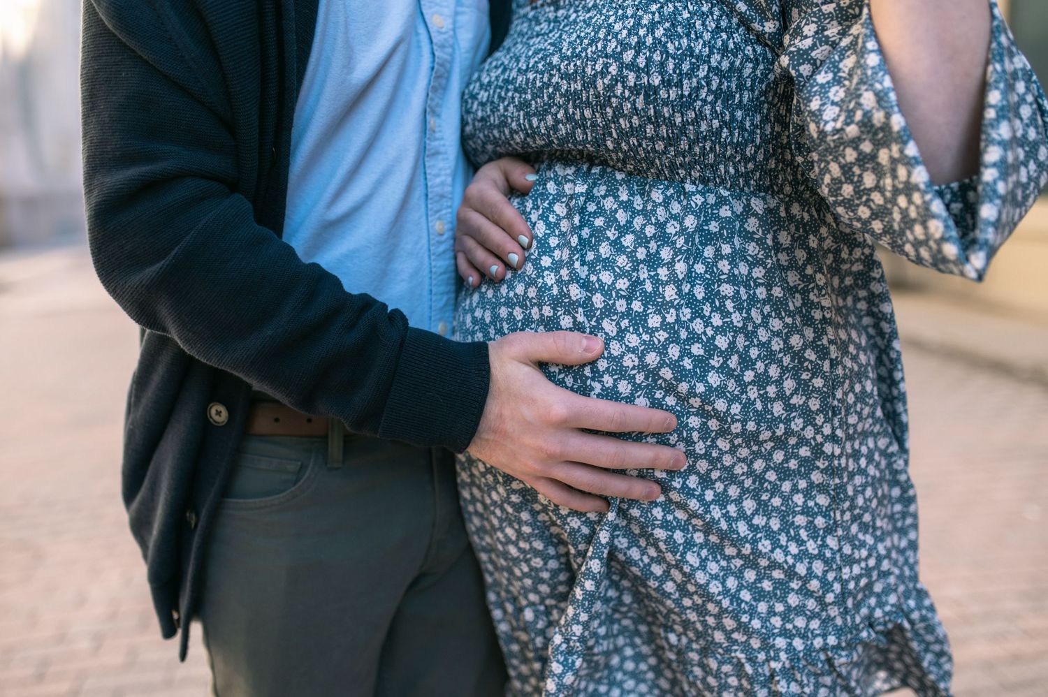 Close-up of hands gently resting on a pregnant belly wearing a blue floral dress.