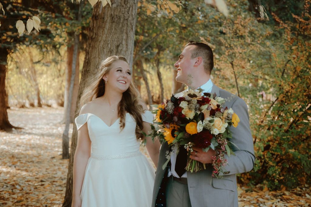 A couple shares a candid moment in an autumn setting with warm sunlight and fall foliage.