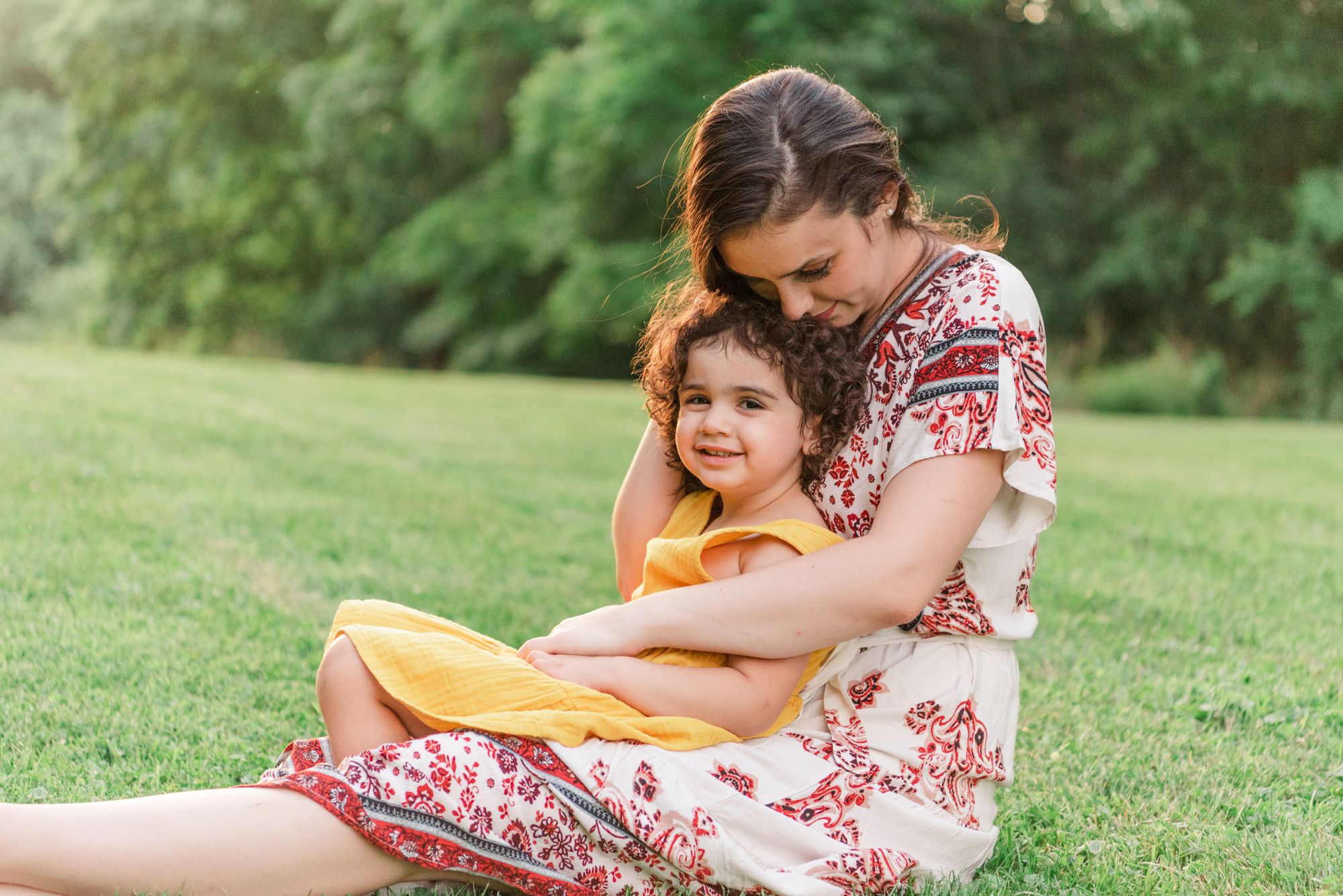 Young girl sitting on mother's lap in field in Pittsburgh, Pennsylvania