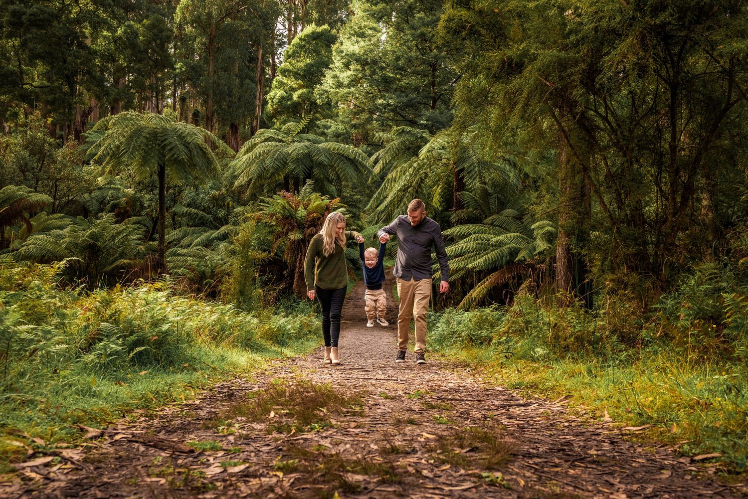 Parents swinging toddler between them on path in forest in Melbourne