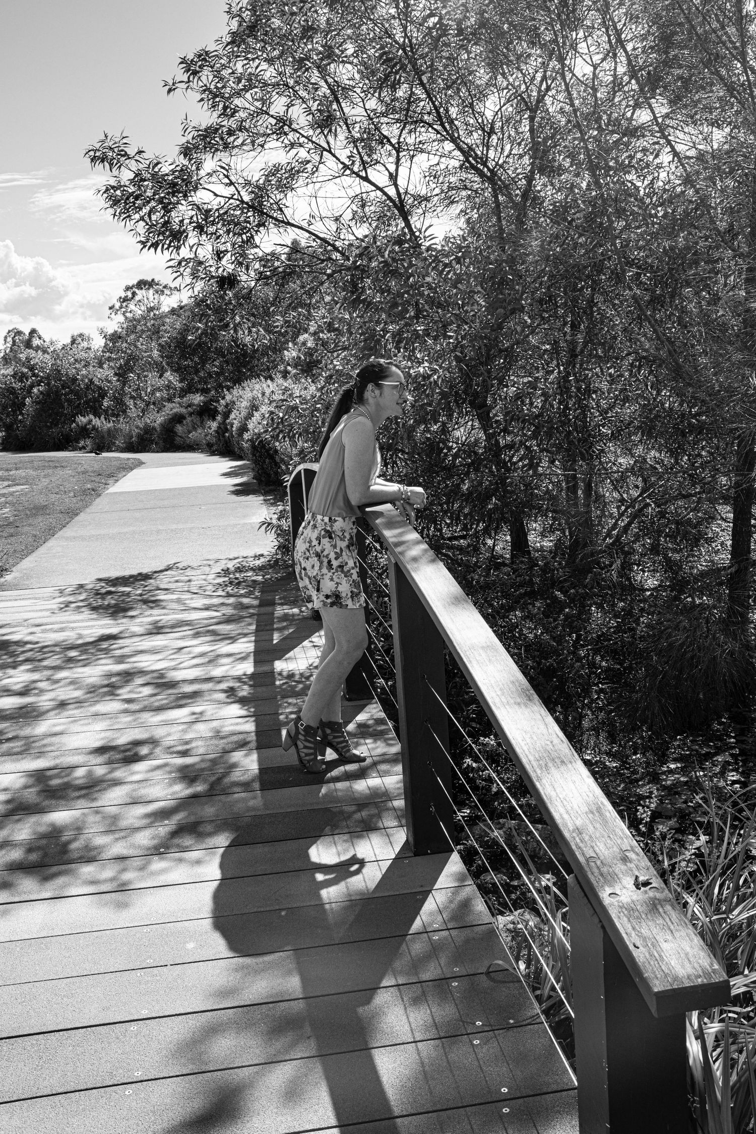 Person looking over wooden bridge railing in black and white photograph.
