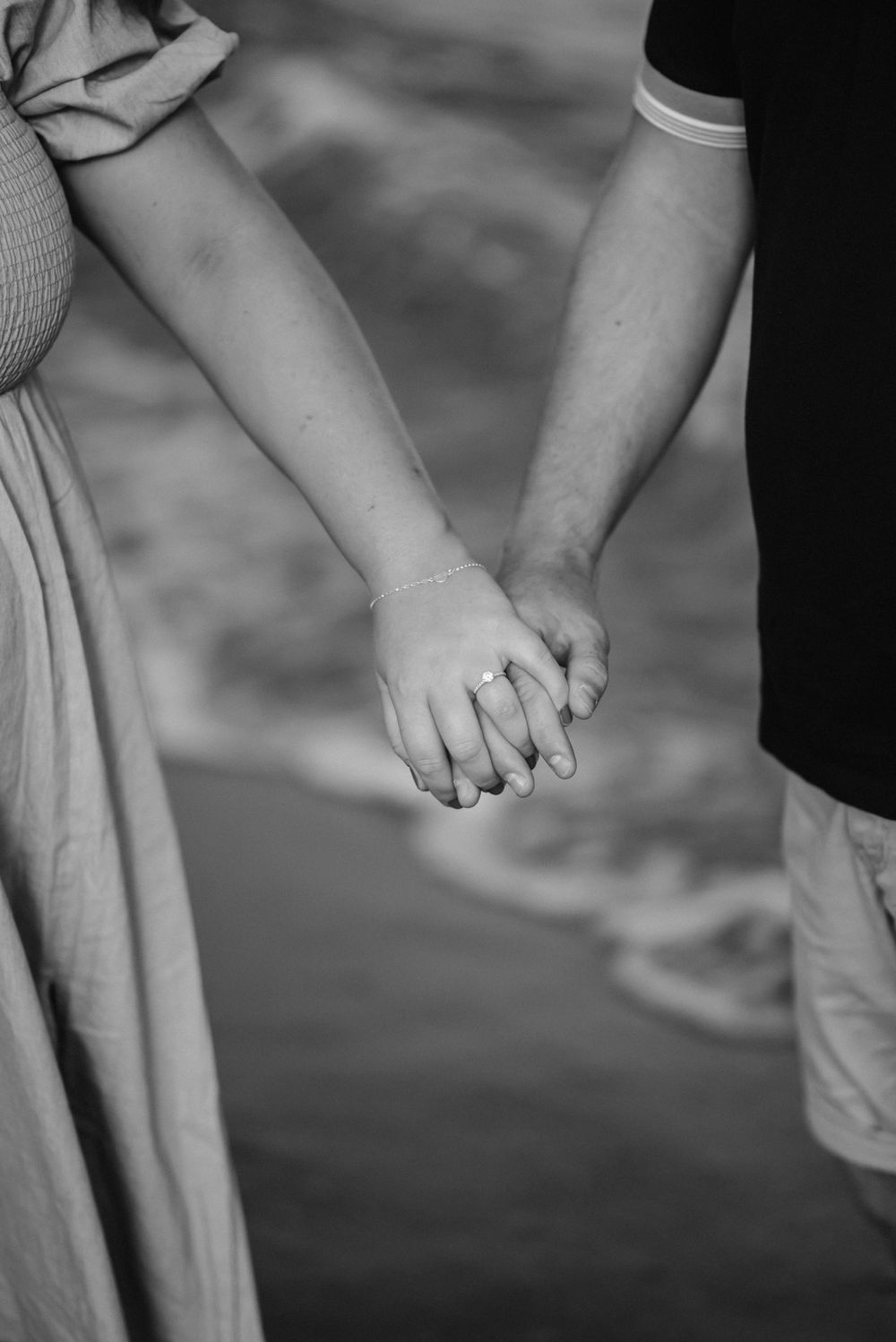 Close-up black and white photo of a couple holding hands outdoors.
