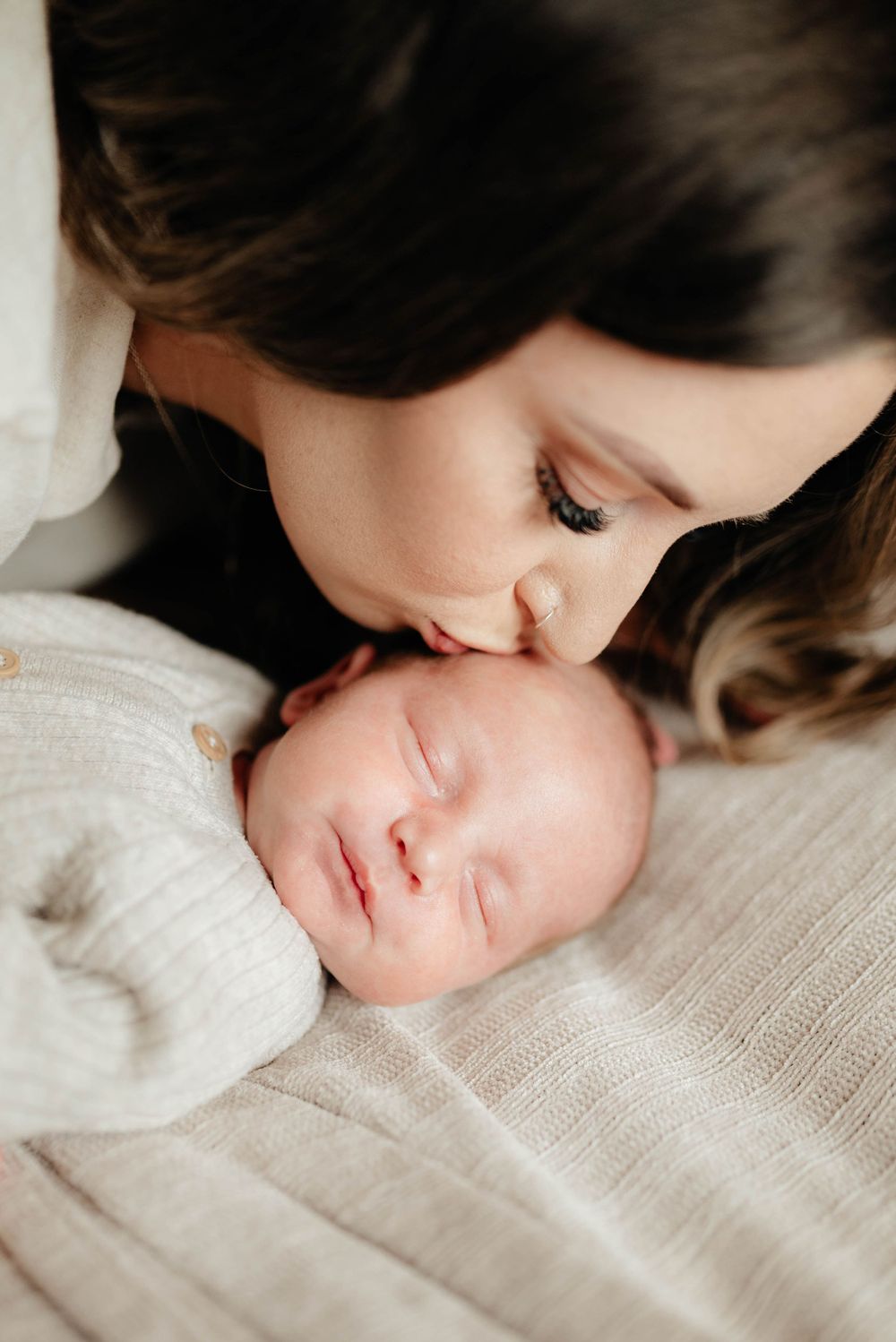 An intimate moment between a mother and sleeping newborn on soft white fabric.