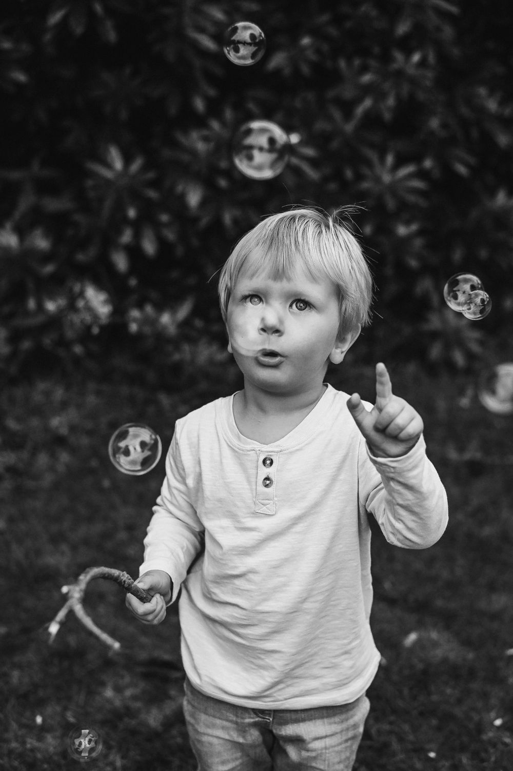A child in a white henley shirt looks up at soap bubbles floating in a black and white photo.