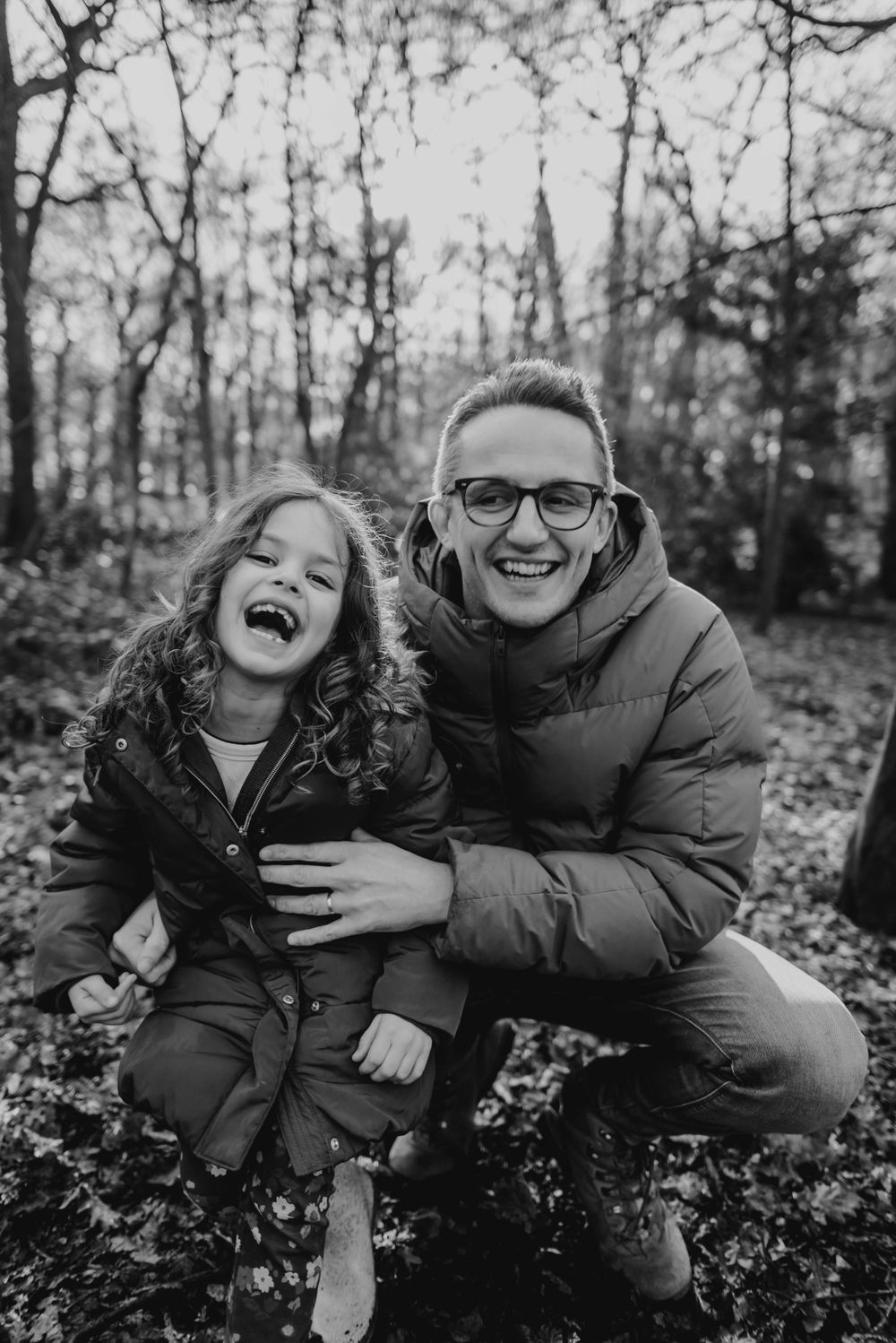 A candid black and white photo capturing laughter between two people in a forest setting.