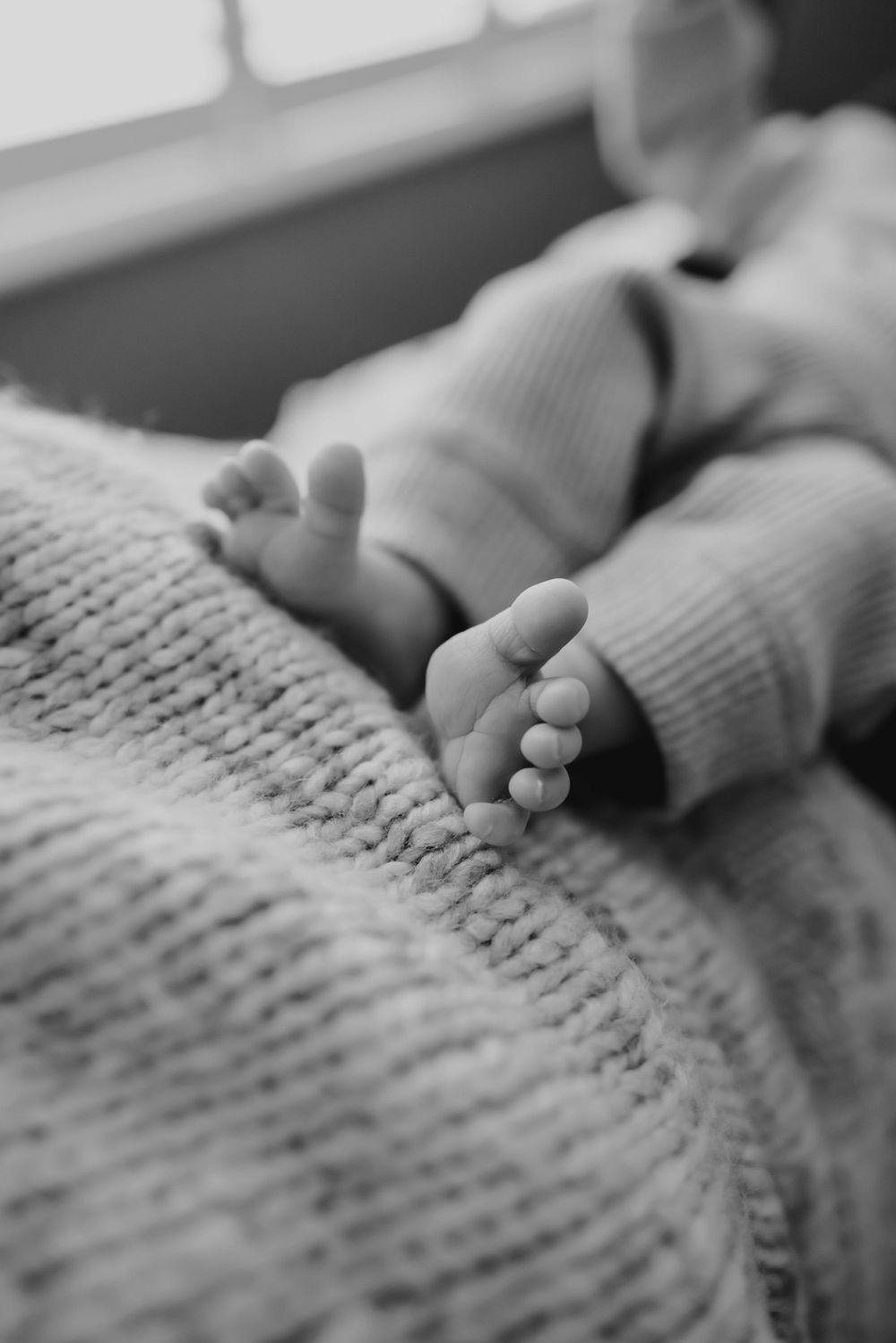 Black and white close-up of tiny baby feet against a knitted blanket.