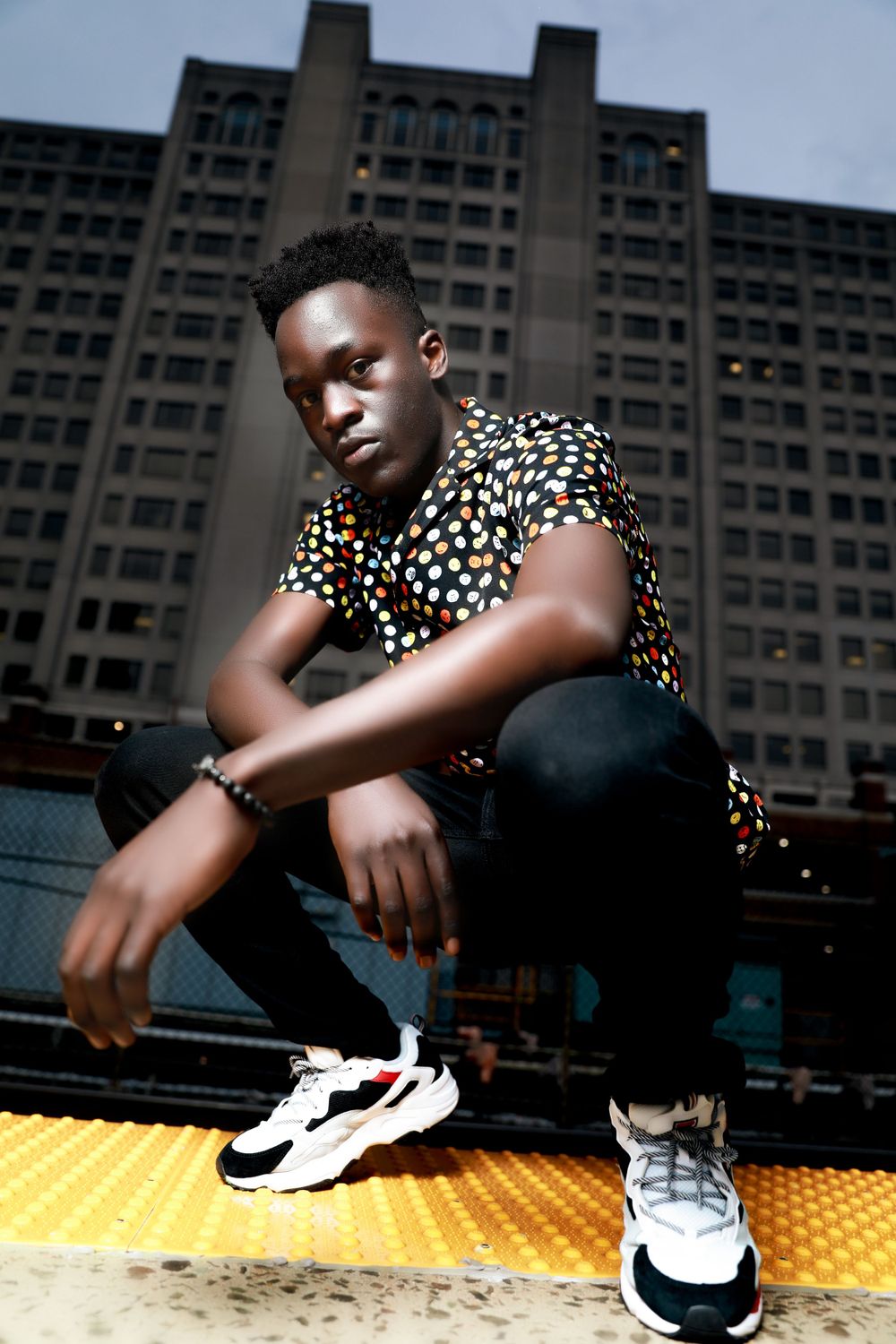 Urban fashion portrait against brutalist architecture featuring polka dot shirt and chunky sneakers.