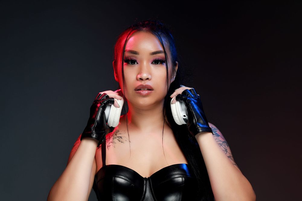 Woman with red and blue hair wearing black outfit and headphones against dark background.