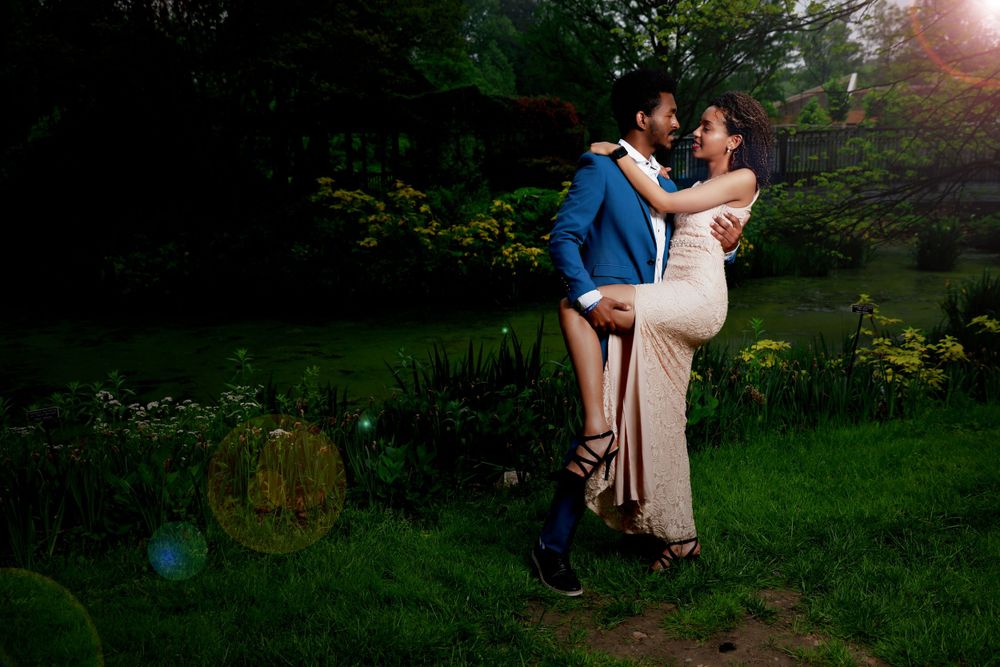 Couple sharing intimate moment in lush garden setting with sun flare effect.
