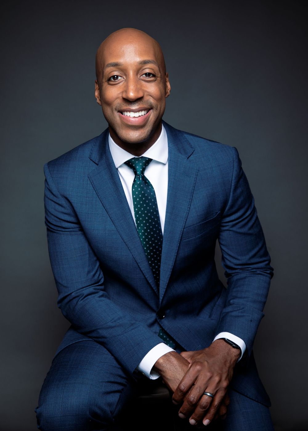 Professional portrait of Anchor for WUSA9 Lorenzo Hall in a blue suit and polka dot tie against a dark background.