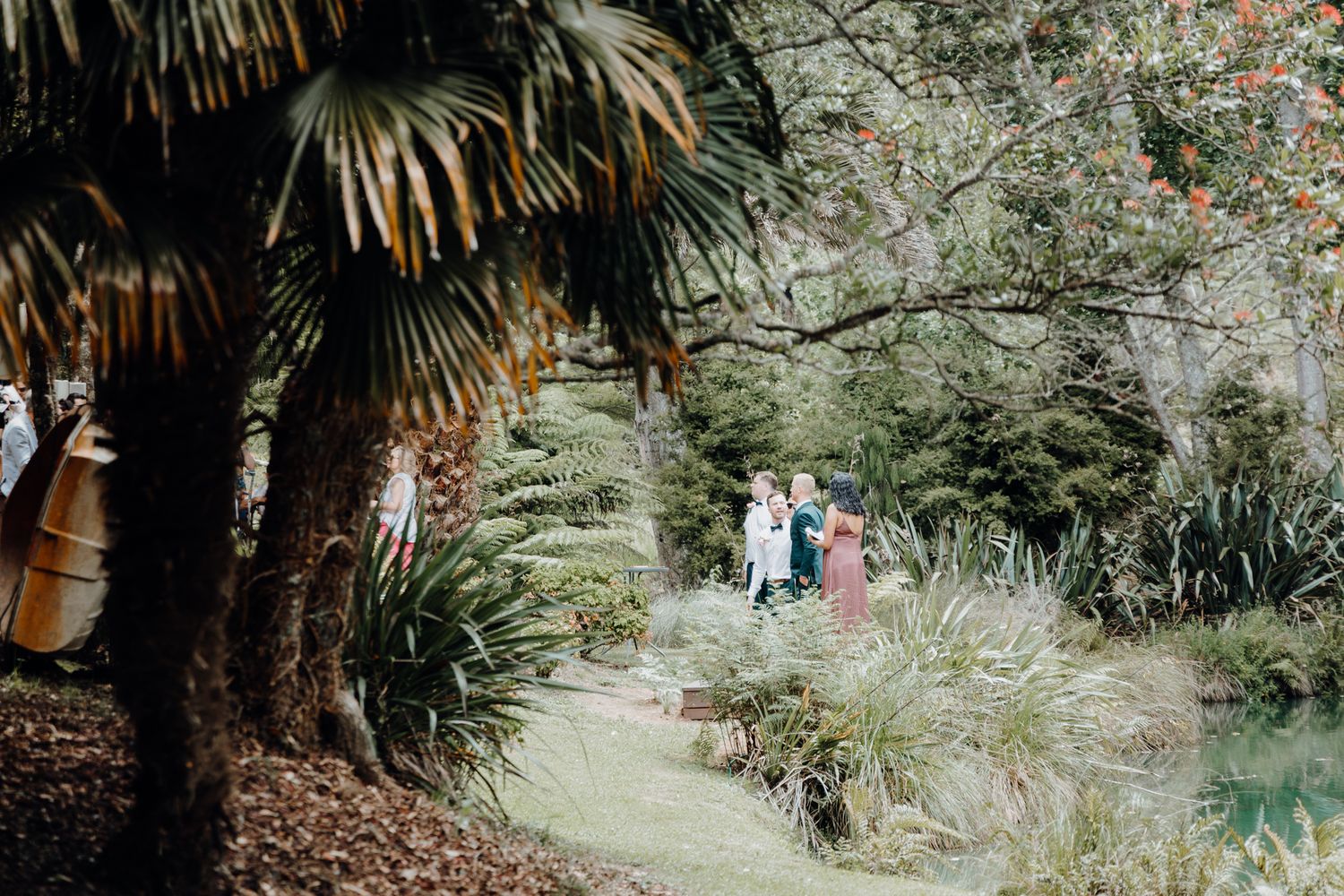 Palm trees frame a distant view of wedding guests walking along a garden path.