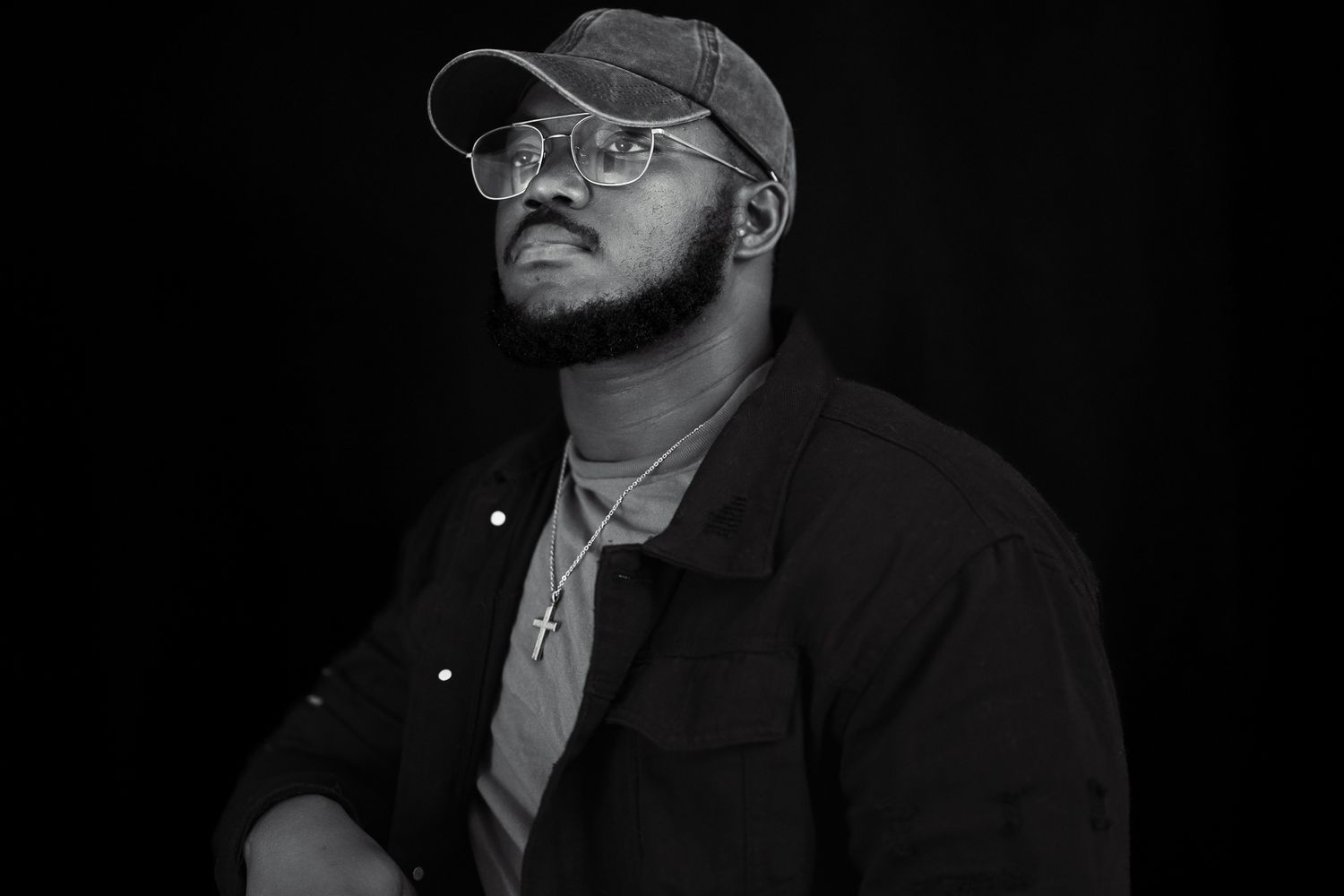 A low-angle black and white portrait of a person in glasses and cap looking contemplative.