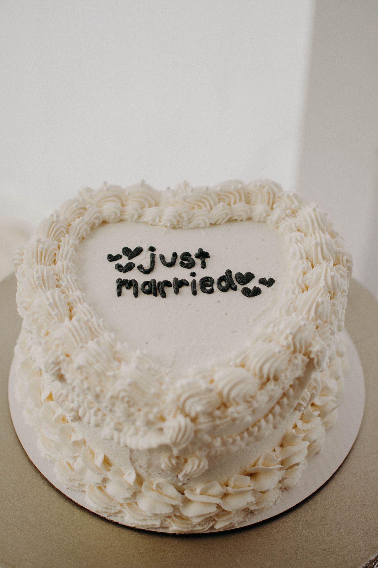 Heart-shaped white wedding cake with piped frosting and 'Just Married' written in black.