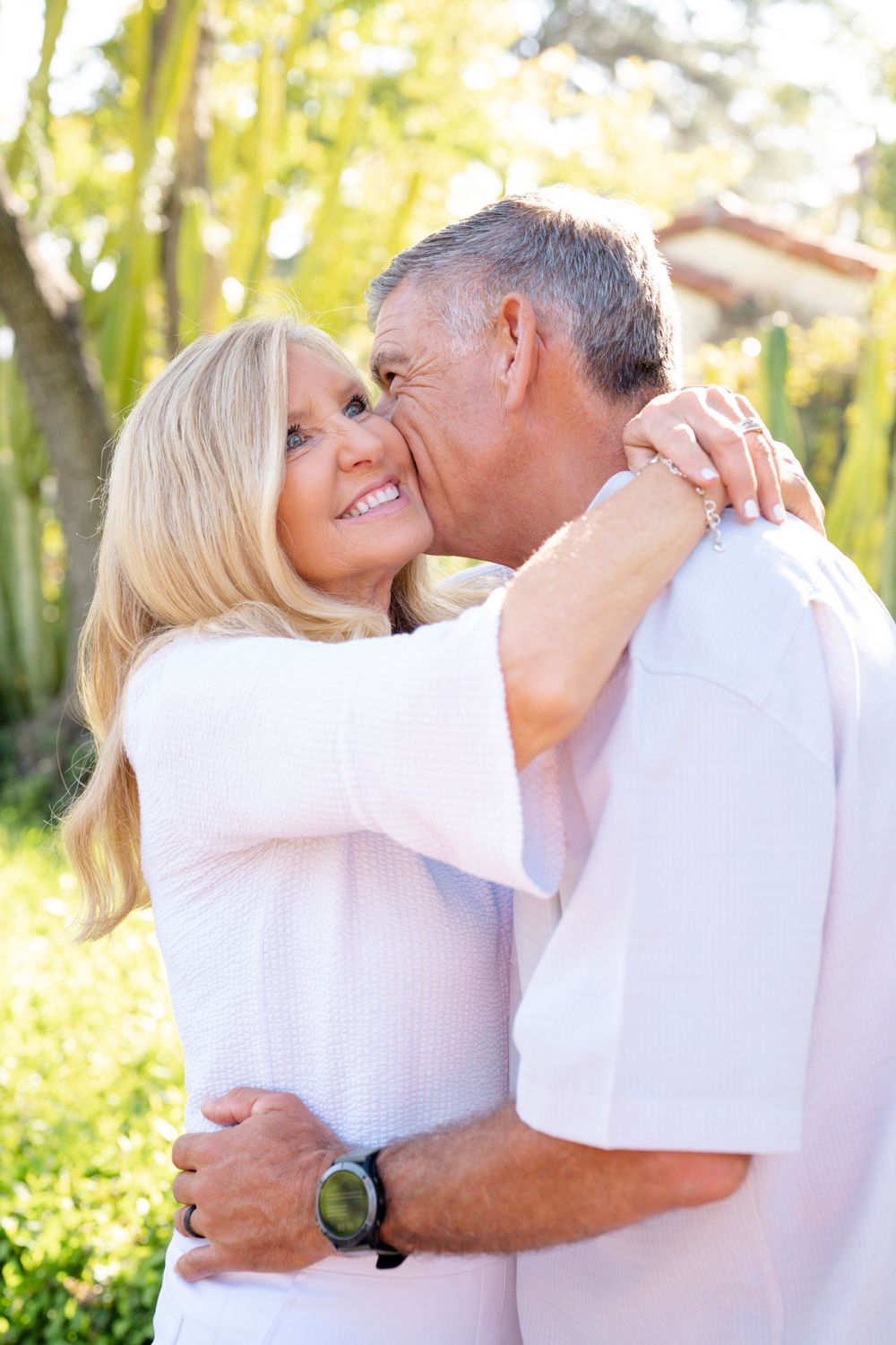 Affectionate couple in white clothing share an intimate moment outdoors in natural sunlight.