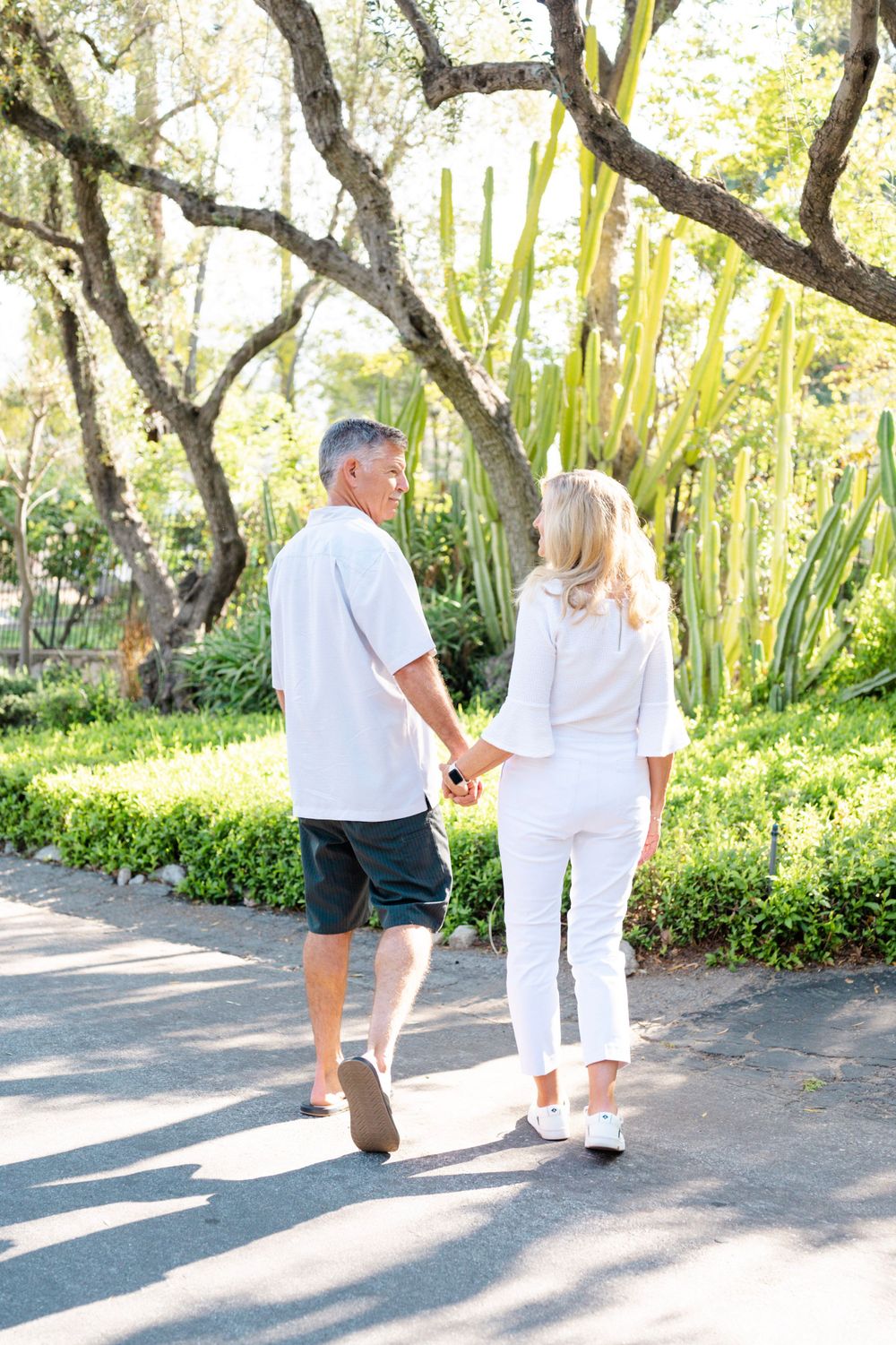 Couple walking hand in hand along a garden path surrounded by lush vegetation.