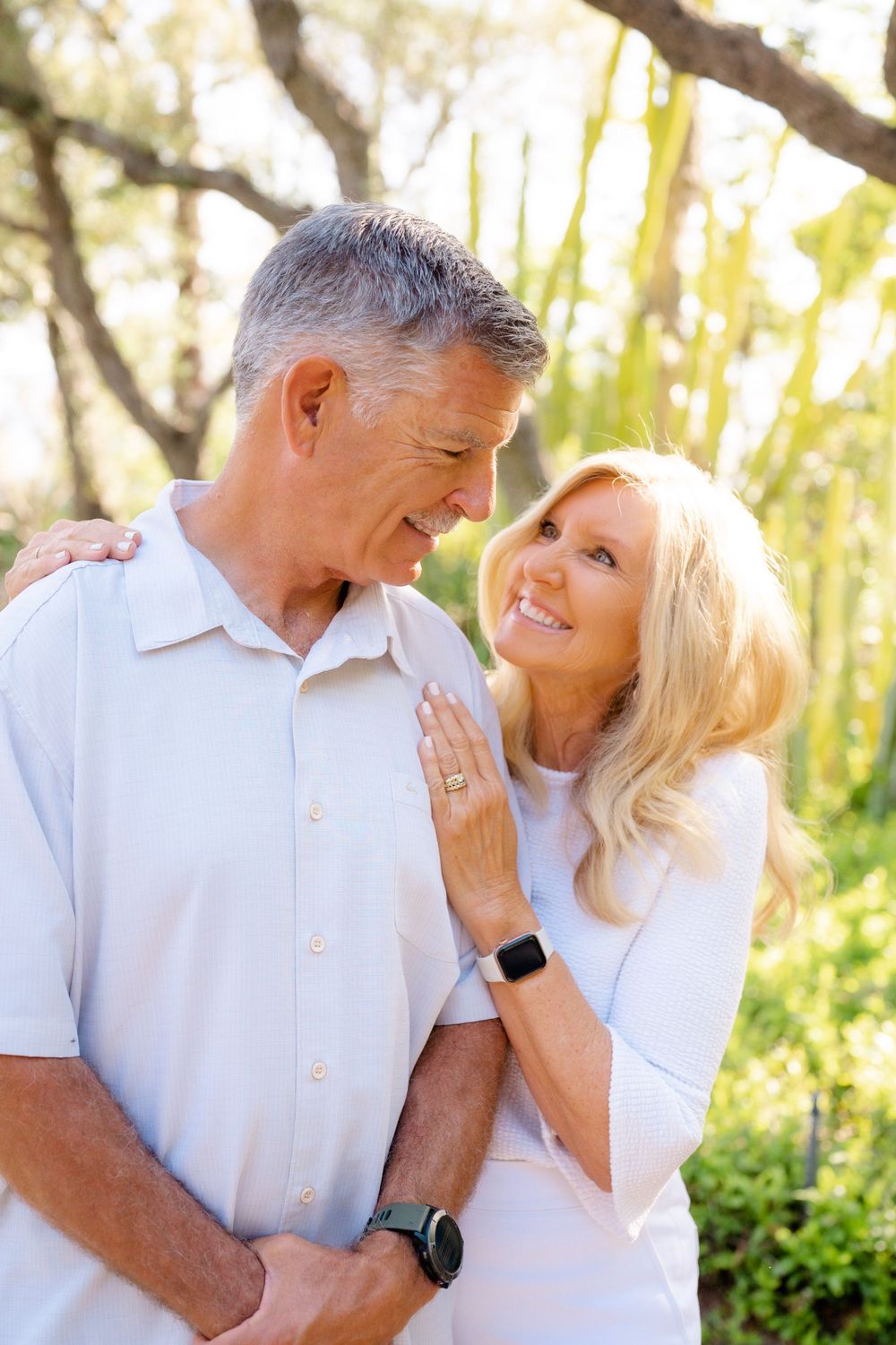 Romantic couple shares a tender moment in a sunlit garden setting while wearing matching white outfits.