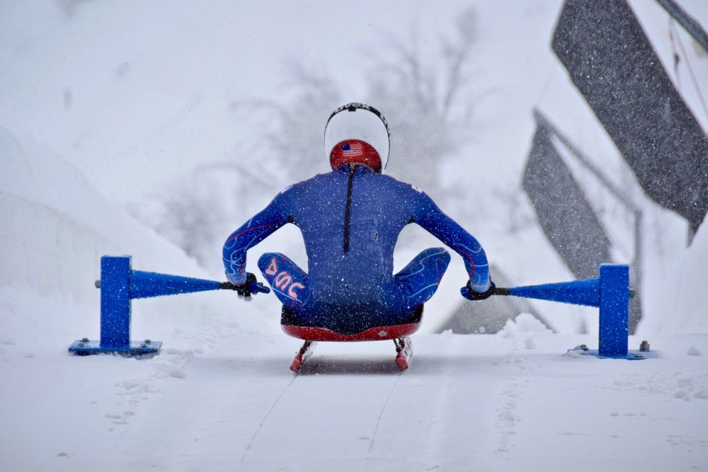 Person in blue winter sportswear doing stretching exercises in snowy conditions.