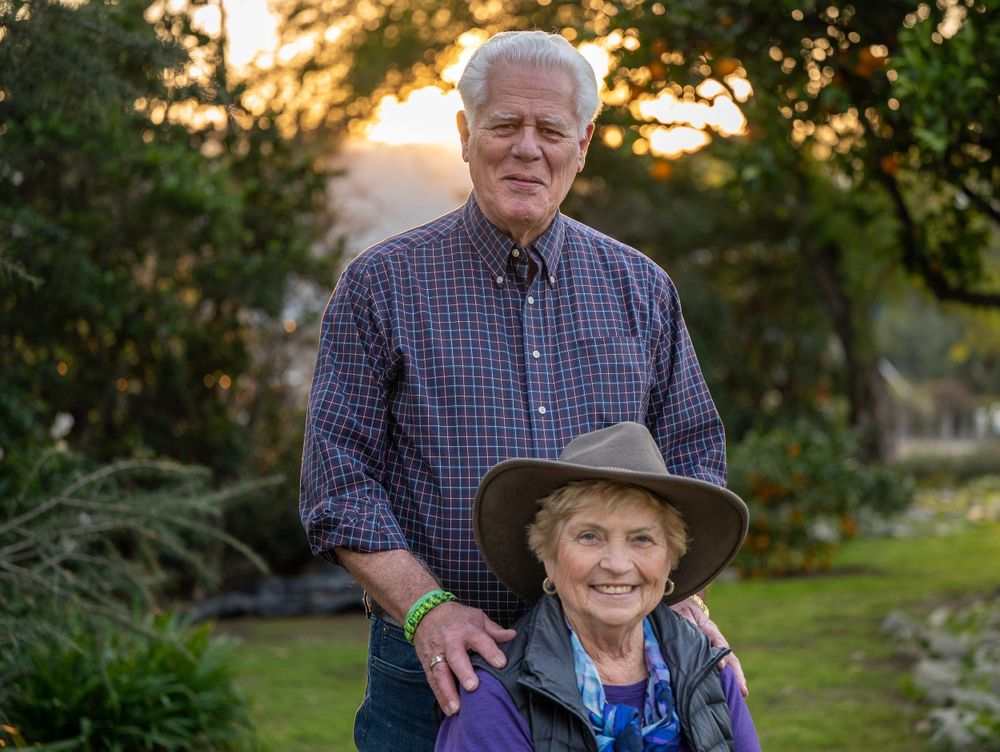 Outdoor portrait of couple in casual attire standing in garden at sunset.
