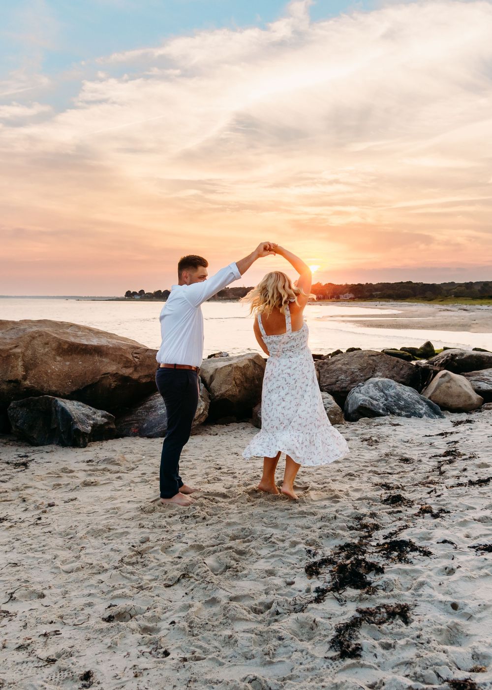 Couple dancing on a rocky beach at sunset with ocean waves in the background.